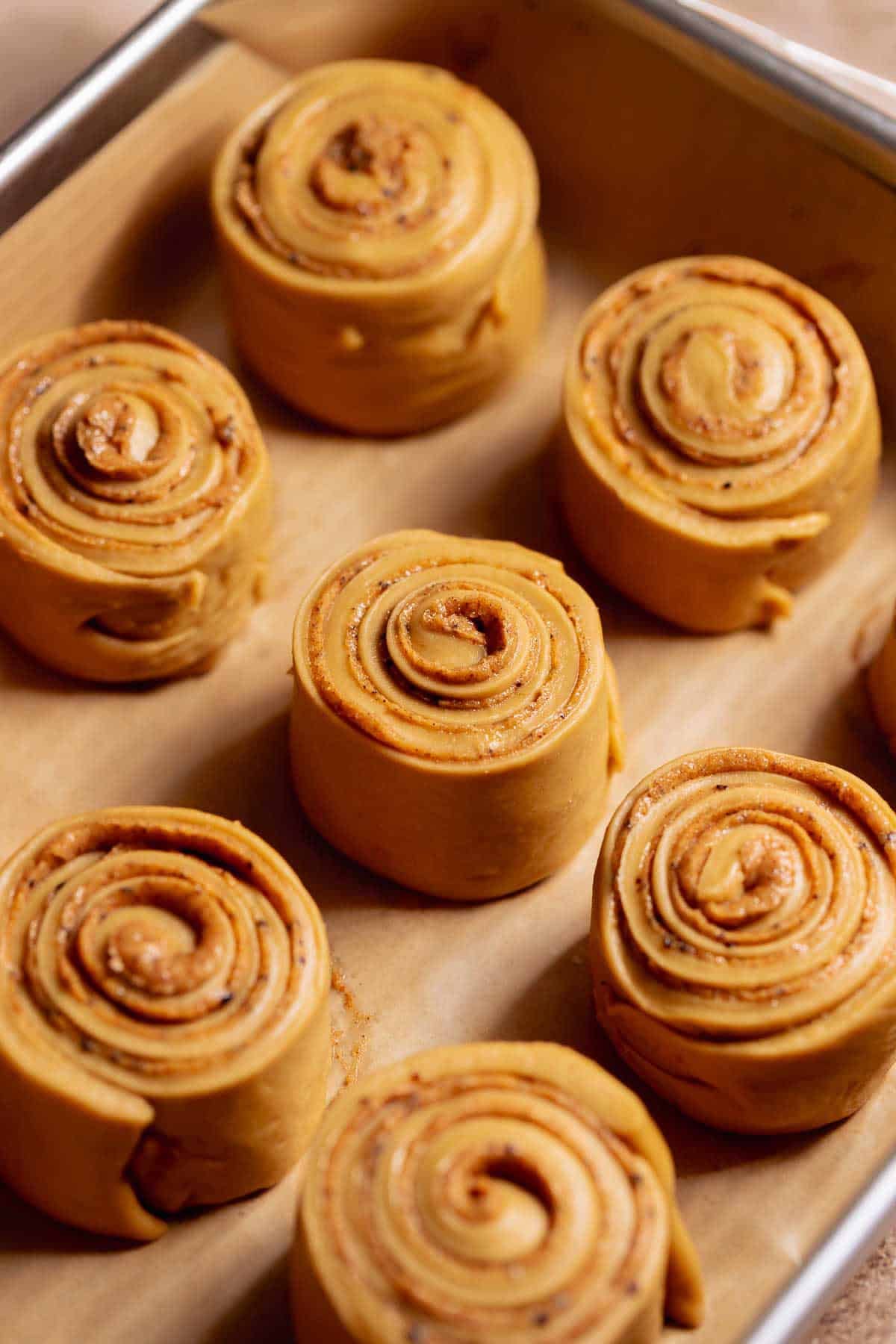 Unbaked coffee cinnamon rolls arranged on a baking tray before rising, showing tight spirals and smooth dough.