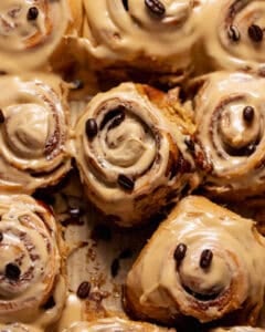 Close-up of espresso cinnamon rolls covered in smooth coffee cream cheese icing with coffee beans sprinkled on top.