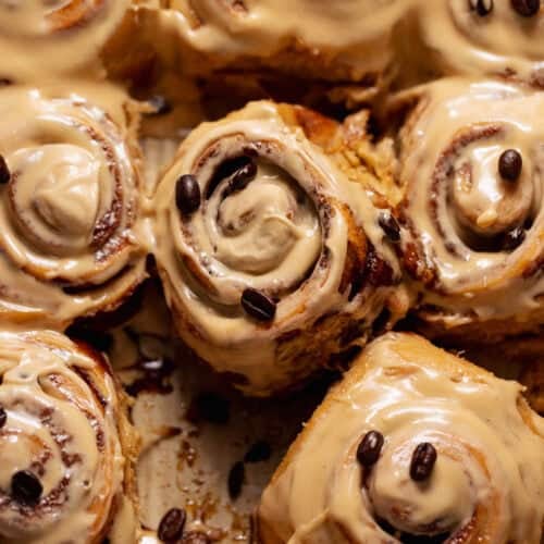 Close-up of espresso cinnamon rolls covered in smooth coffee cream cheese icing with coffee beans sprinkled on top.