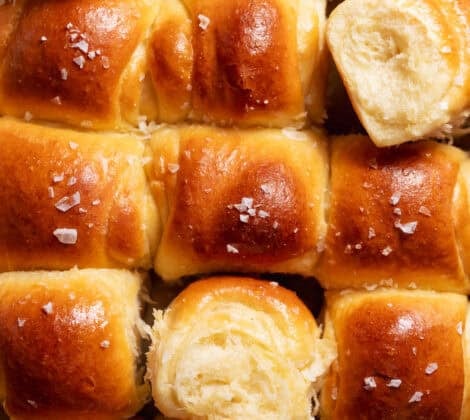 Golden brown milk bread dinner rolls baked in a square pan with flaky sea salt on top.