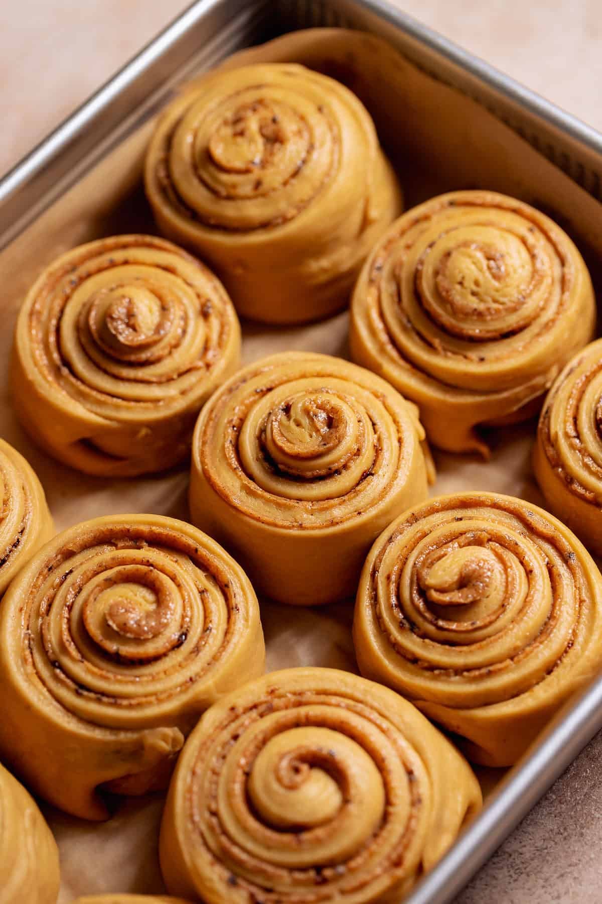 Proofed cinnamon rolls after rising, soft and puffy with visible coffee cinnamon swirls in a baking pan.