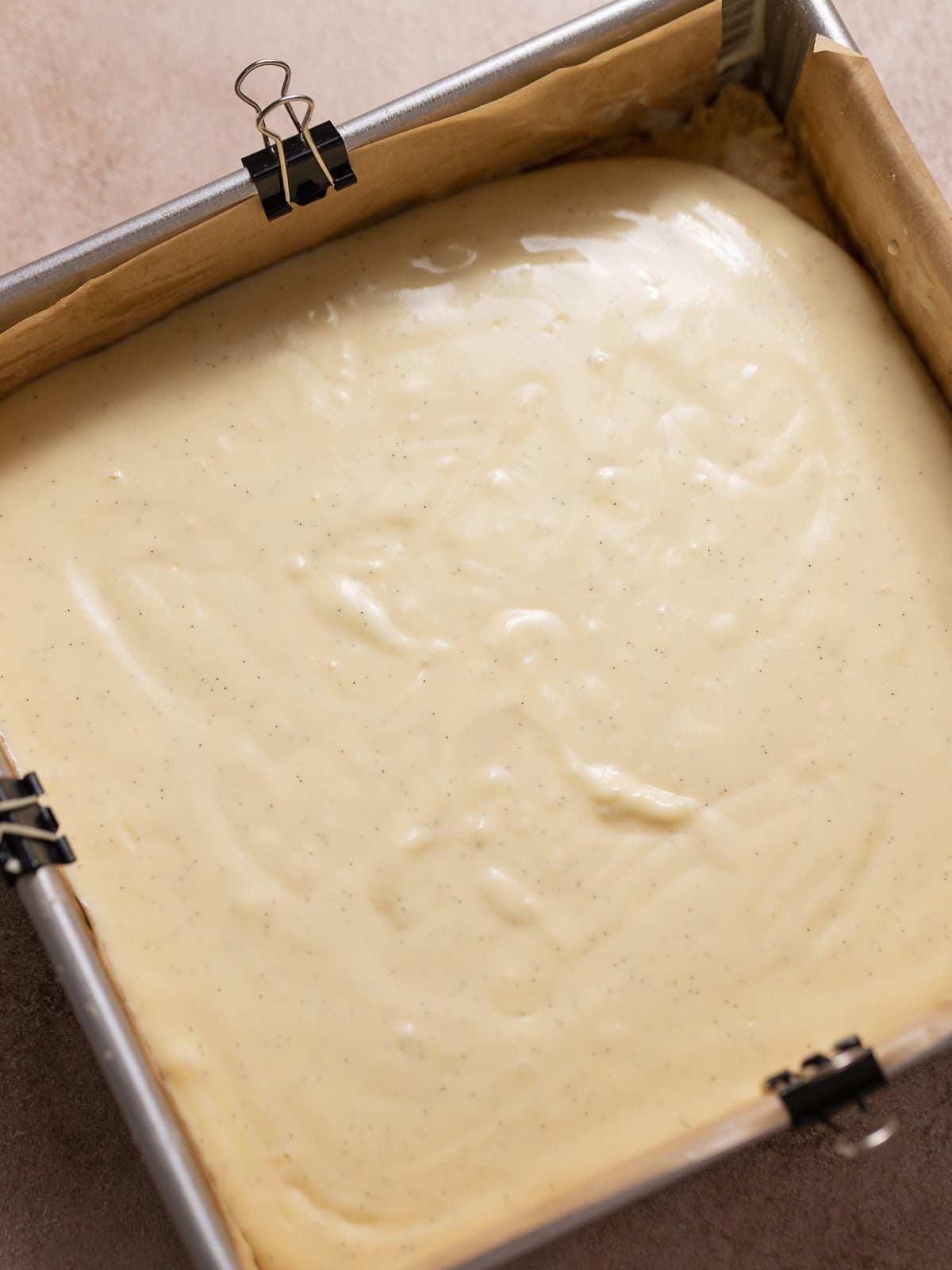 Vanilla cheesecake batter poured over the shortbread crust in a baking pan.