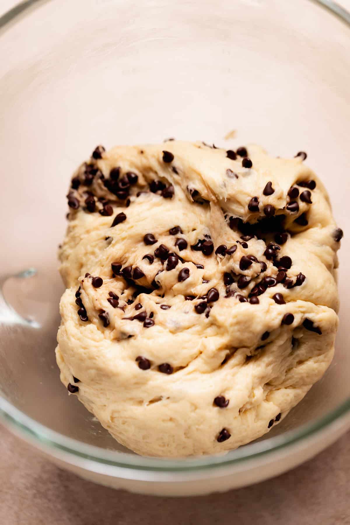 Soft enriched yeast dough mixed with mini chocolate chips resting in a glass bowl.