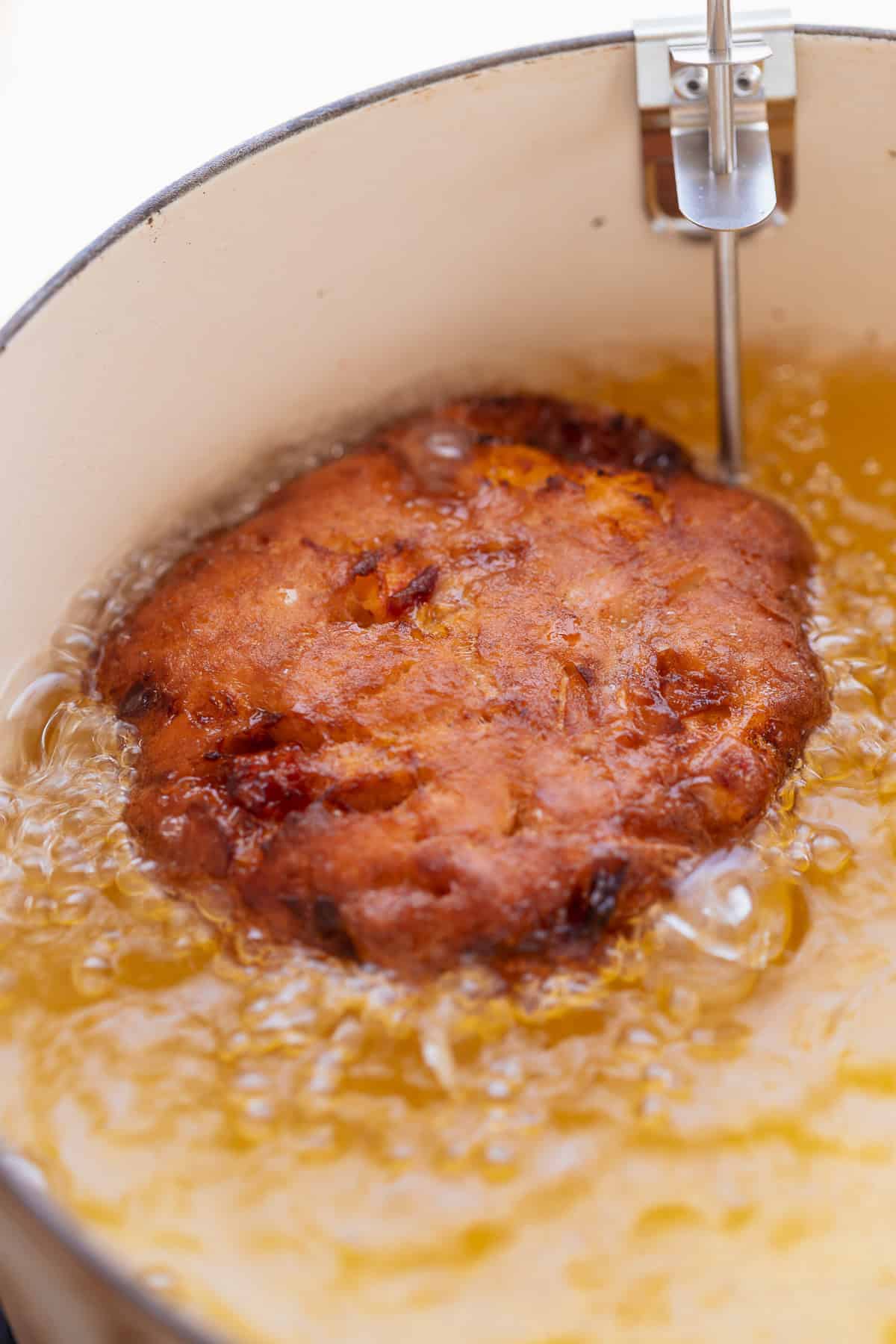 A fritter frying in hot oil until golden brown and crispy.