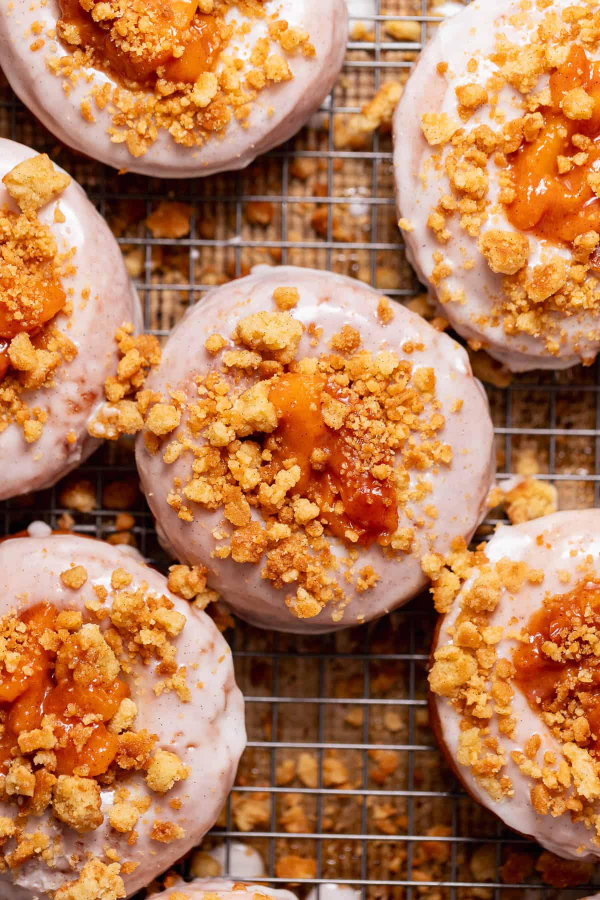 Peach cobbler donuts with cinnamon glaze, peach filling, and buttery crumble topping on a cooling rack.