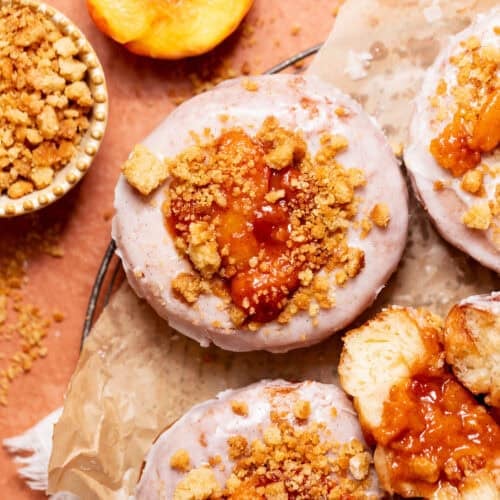Overhead view of peach cobbler donuts with cinnamon glaze, peach topping, and buttery crumble topping.