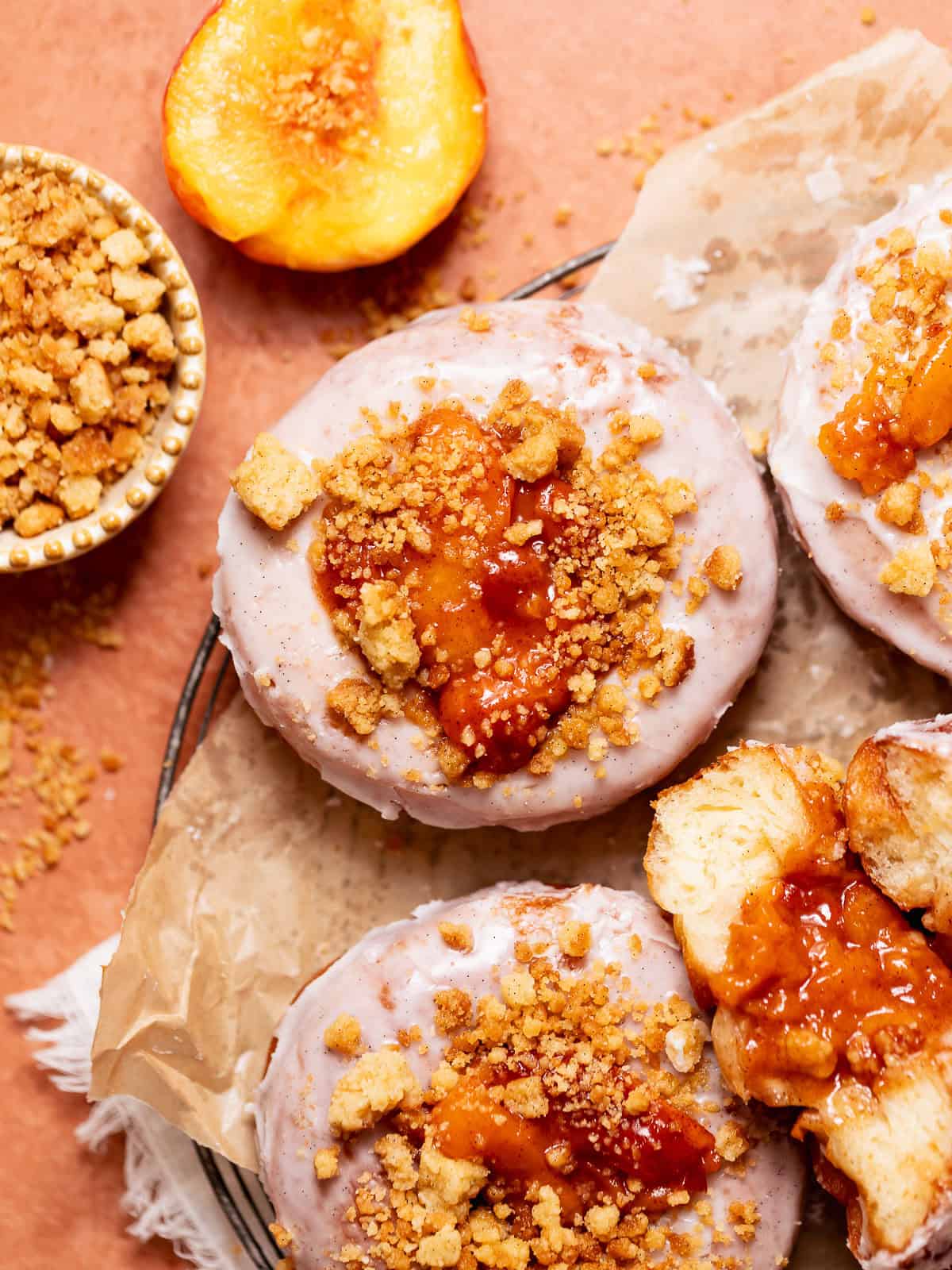 Overhead view of peach cobbler donuts with cinnamon glaze, peach topping, and buttery crumble topping.