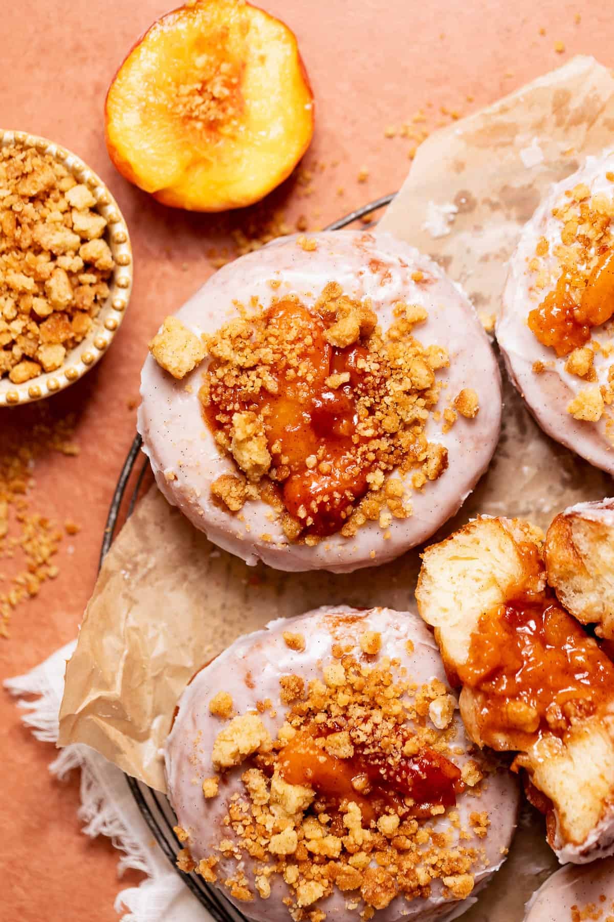 Peach cobbler donuts with peach filling, cinnamon glaze, and buttery crumble topping on a cooling rack.