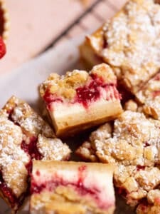 Strawberry cheesecake crumb bars dusted with powdered sugar on a wire rack.