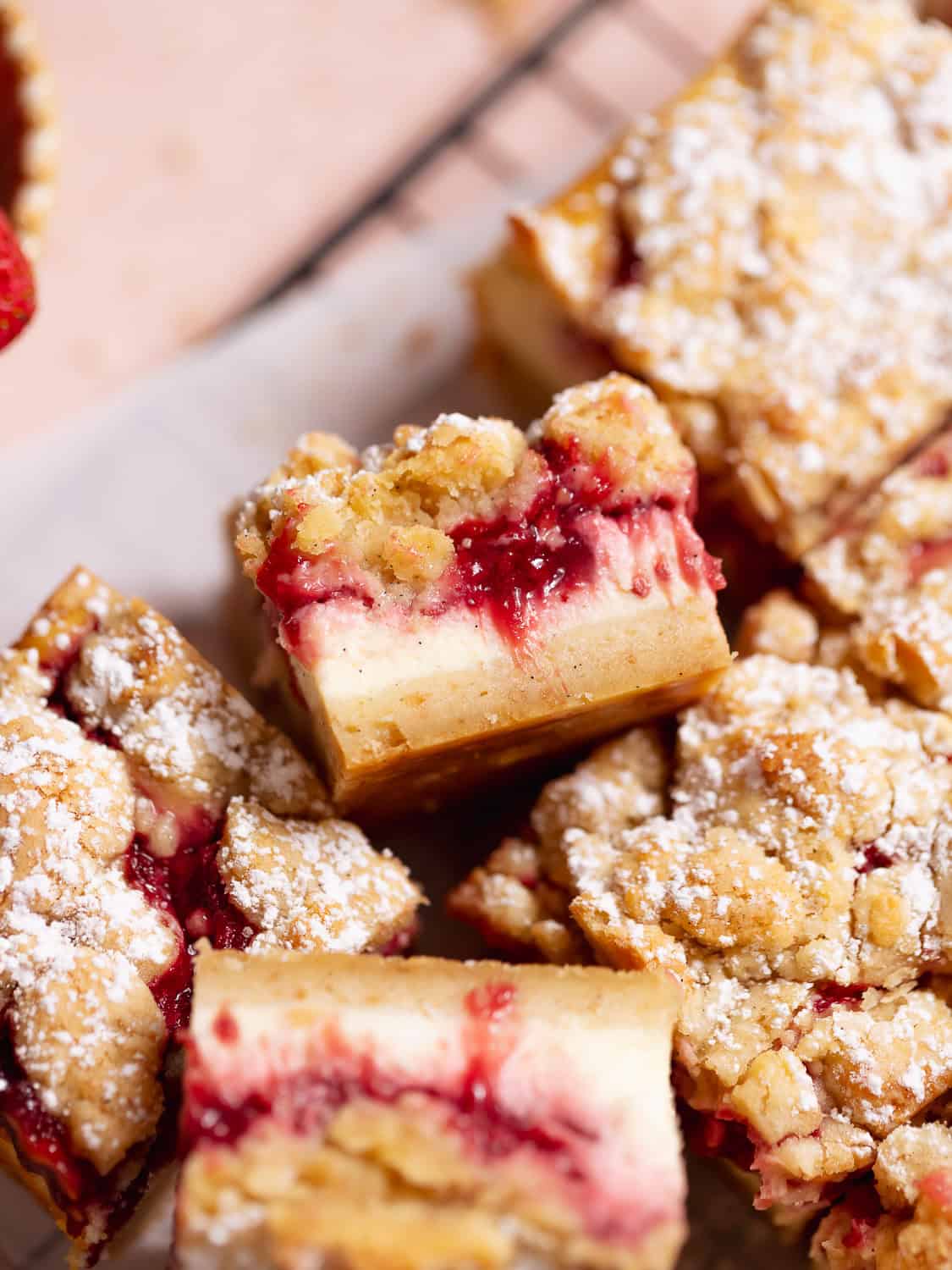 Strawberry cheesecake crumb bars dusted with powdered sugar on a wire rack.