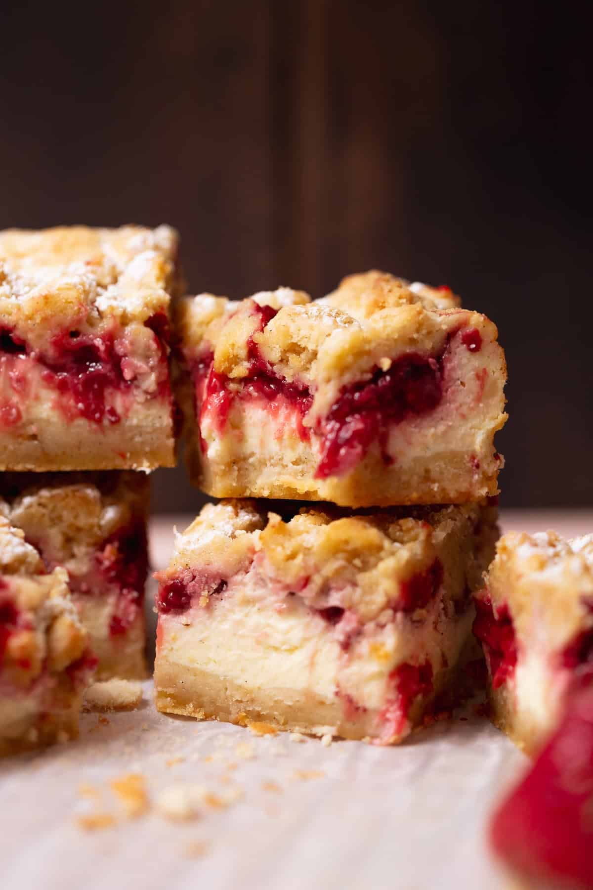 Close-up bite shot of strawberry cheesecake bars stacked on parchment paper.