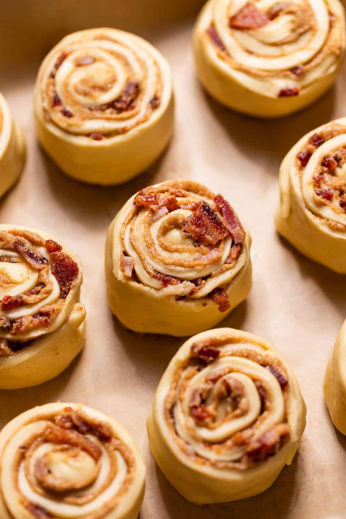 Assembled bacon cinnamon rolls arranged in a parchment-lined baking pan.