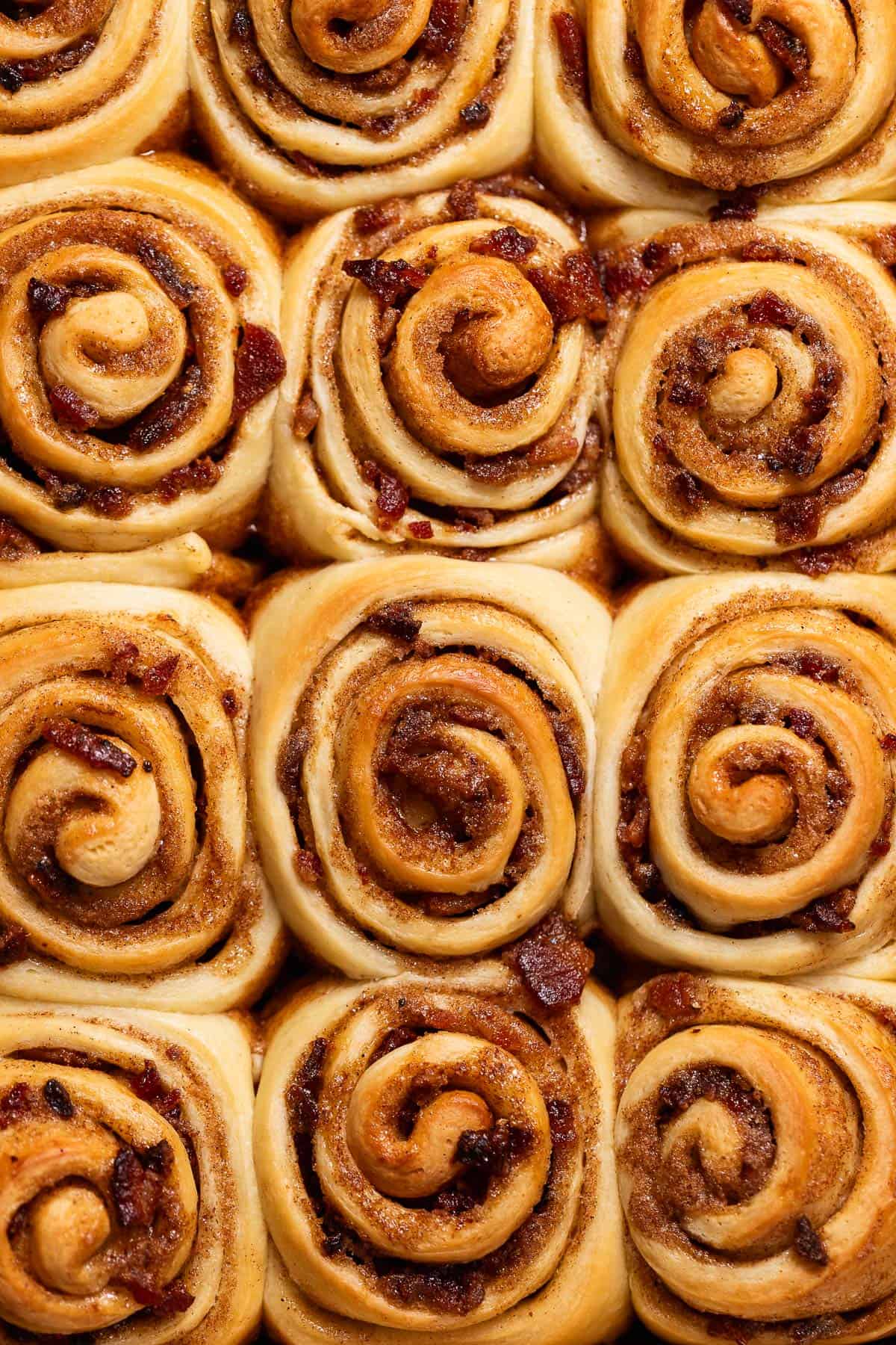 Freshly baked bacon cinnamon rolls with visible candied bacon pieces.