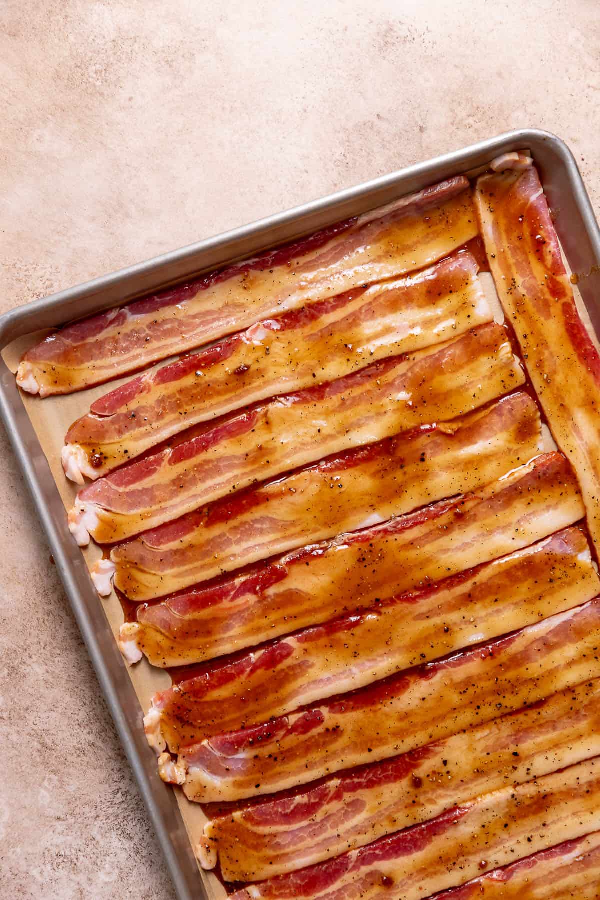 Maple-glazed bacon strips on a sheet pan before baking to caramelize it.