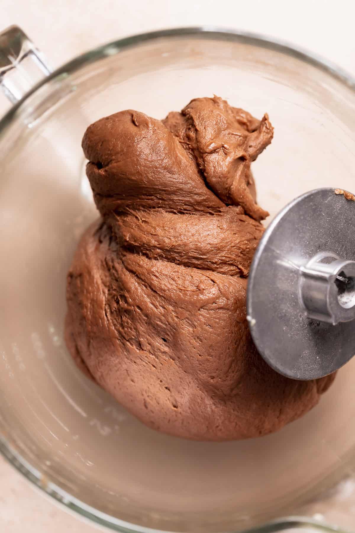 Kneaded chocolate cinnamon roll dough in a glass mixer bowl after mixing, smooth and elastic with a rich chocolate color.