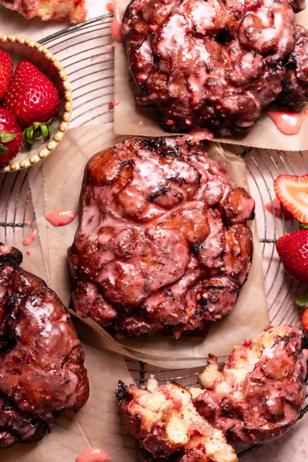 Strawberry fritters topped with a fresh strawberry glaze, served on parchment paper with fresh strawberries and a torn fritter showing the soft interior.