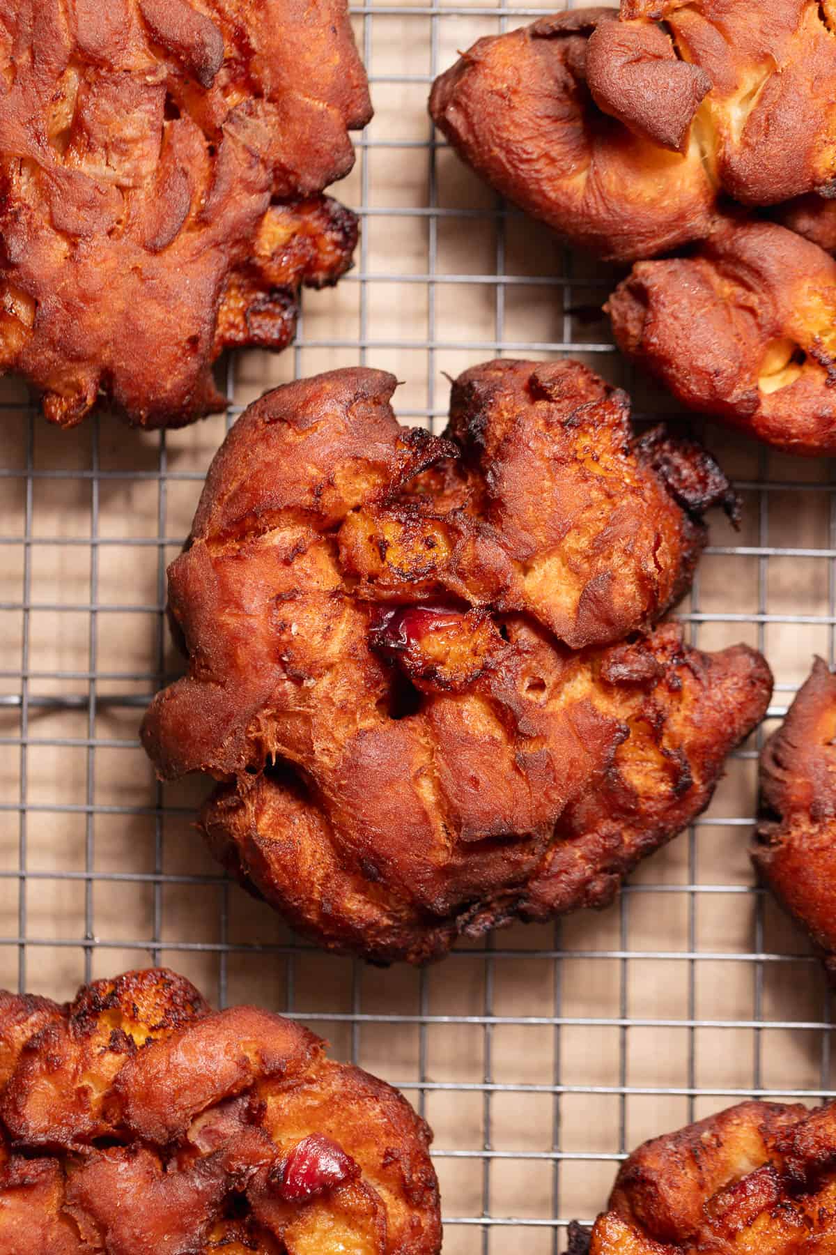 Homemade peach fritters fresh from the fryer cooling on a wire rack before glazing.