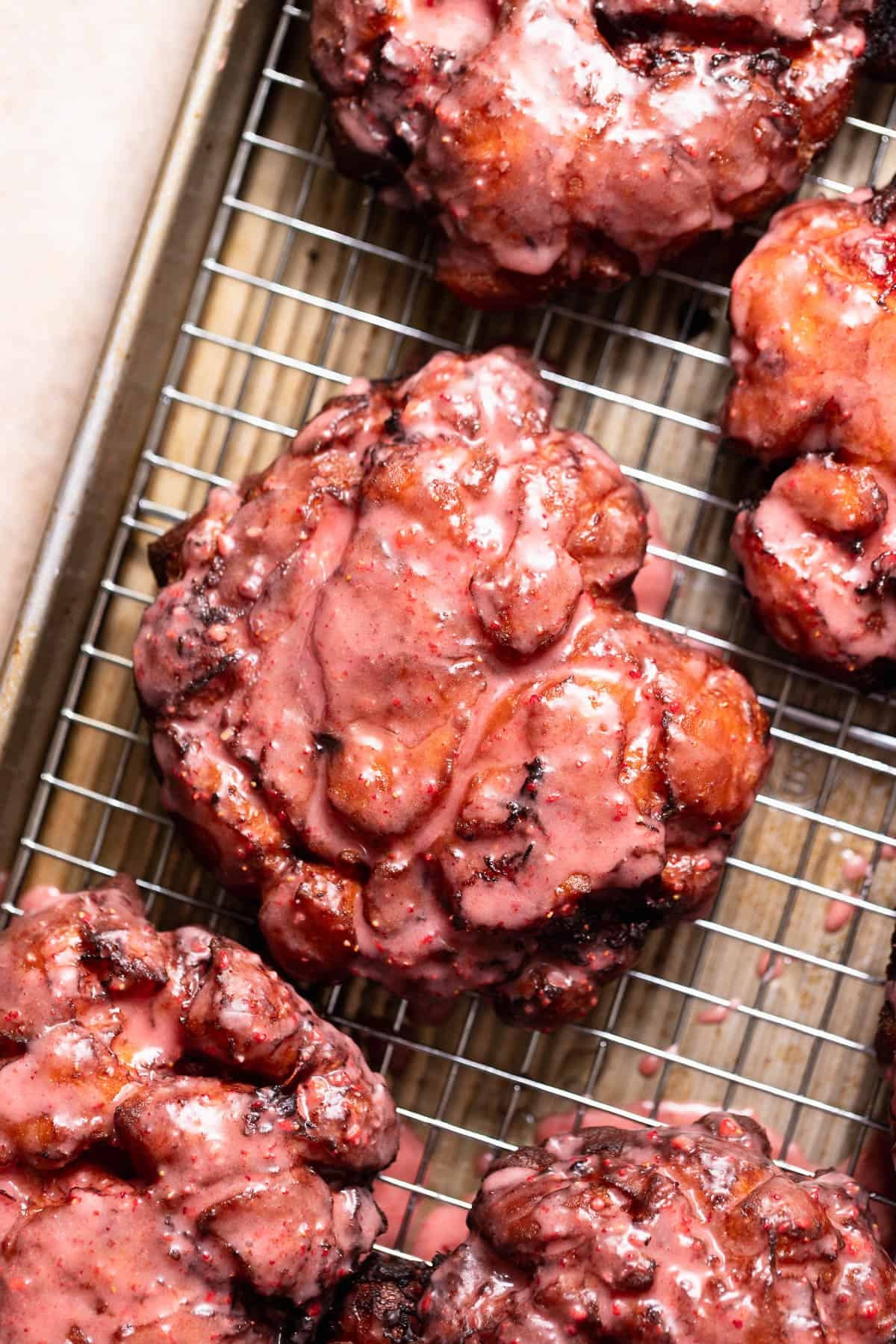 Homemade fried fritters coated in a strawberry glaze on a cooling rack.