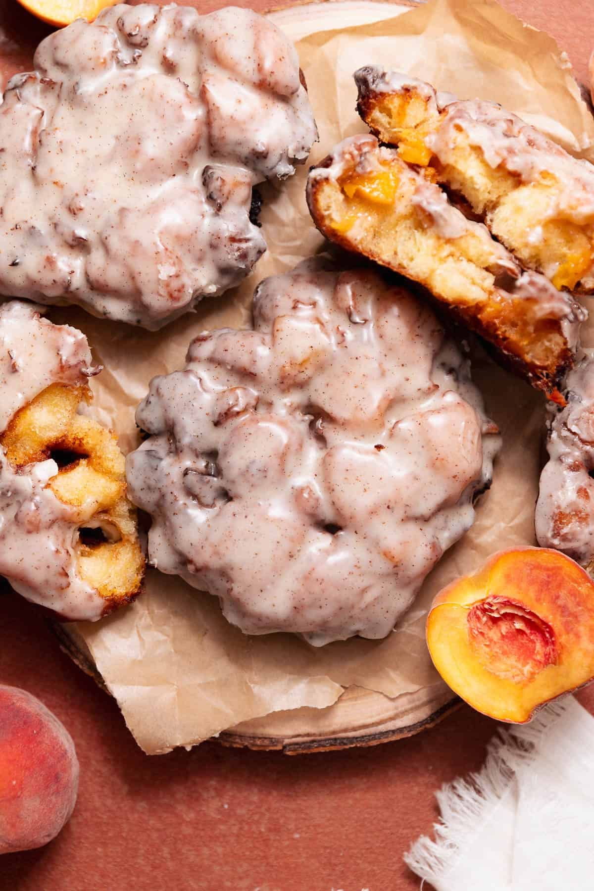 Homemade peach fritters topped with brown butter glaze, served with fresh peaches and a fritter broken open to show the soft peach-filled interior.