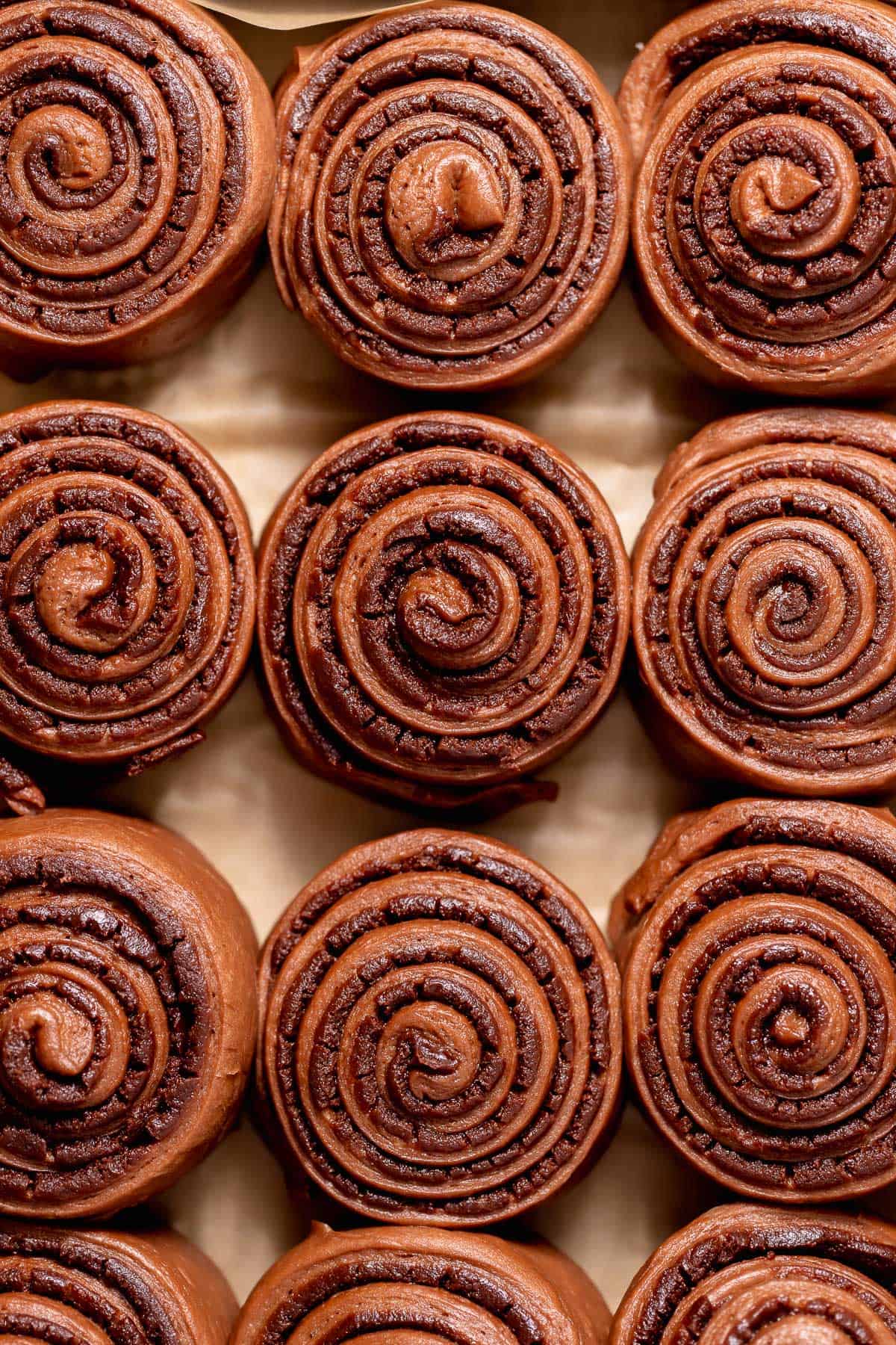 Proofed chocolate brownie rolls in a parchment-lined baking pan, showing their soft, risen swirls before baking.