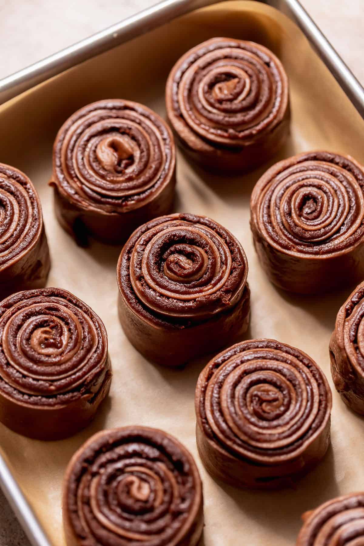 Chocolate dough with brownie filling rolled into tight swirls arranged in a baking pan.
