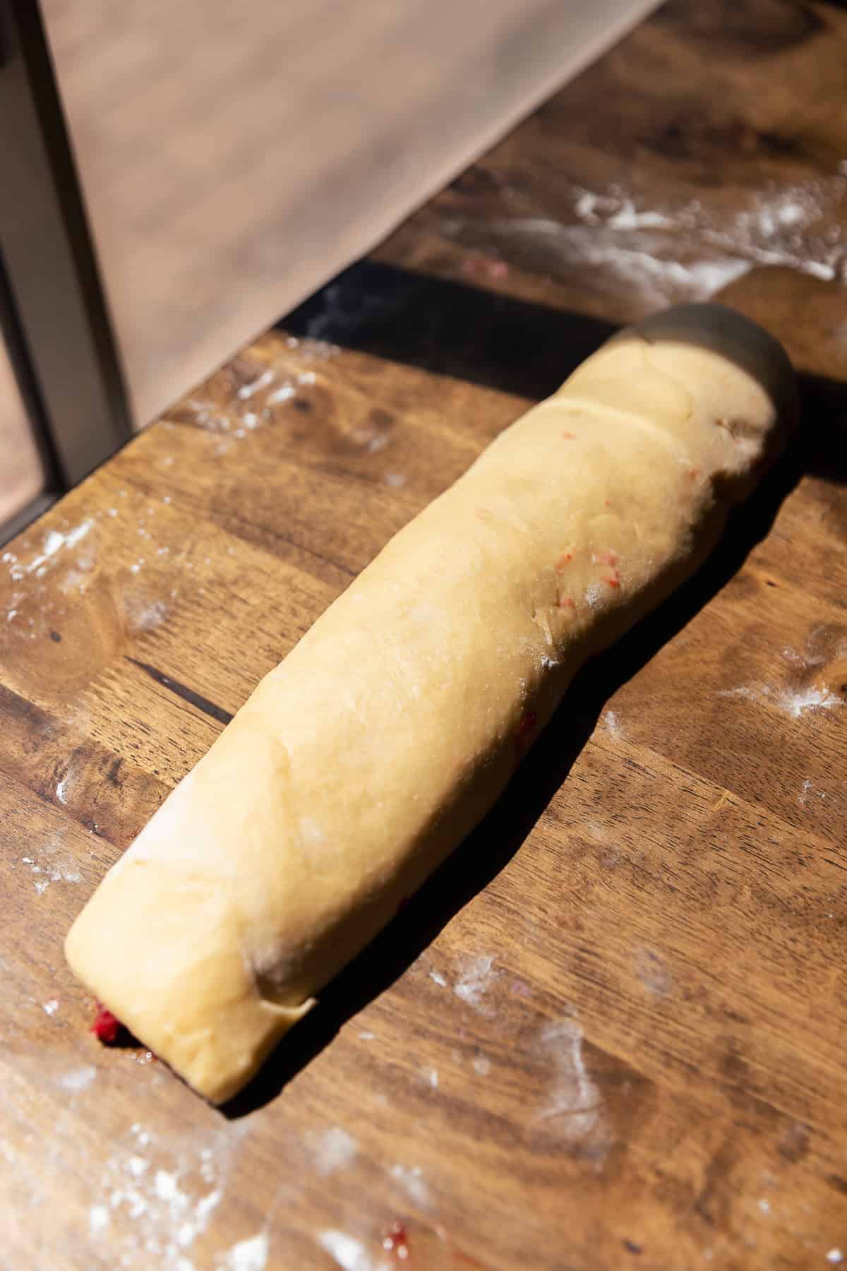 Rolled log of strawberry fritter dough before cutting and shaping.