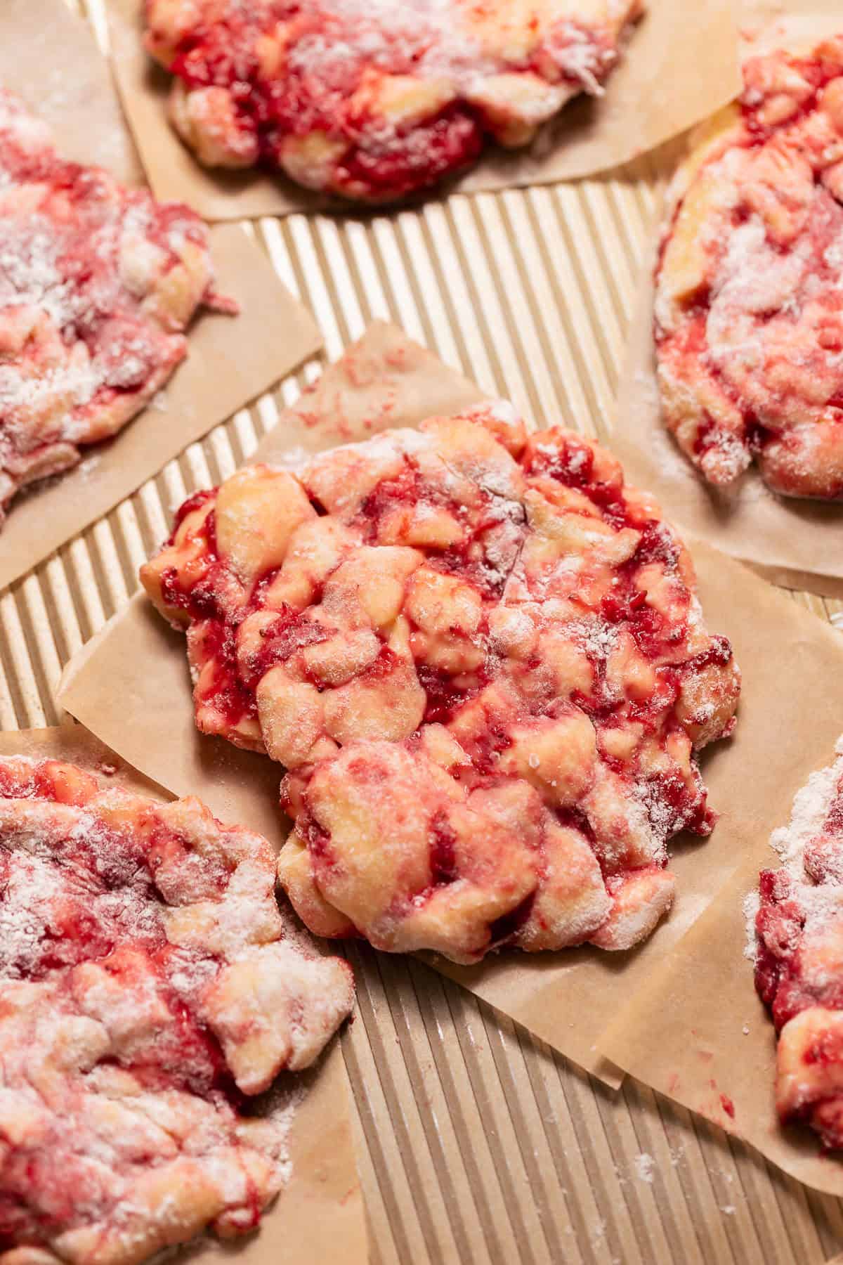 Unfried strawberry fritters on parchment paper squares dusted with flour and ready for frying.