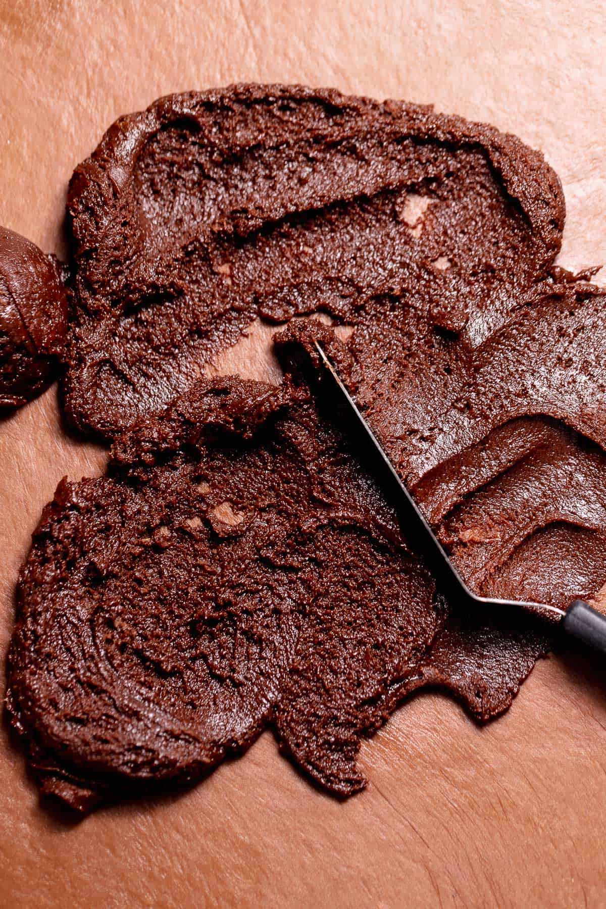 Chocolate brownie filling spread across rolled chocolate dough with a spatula.