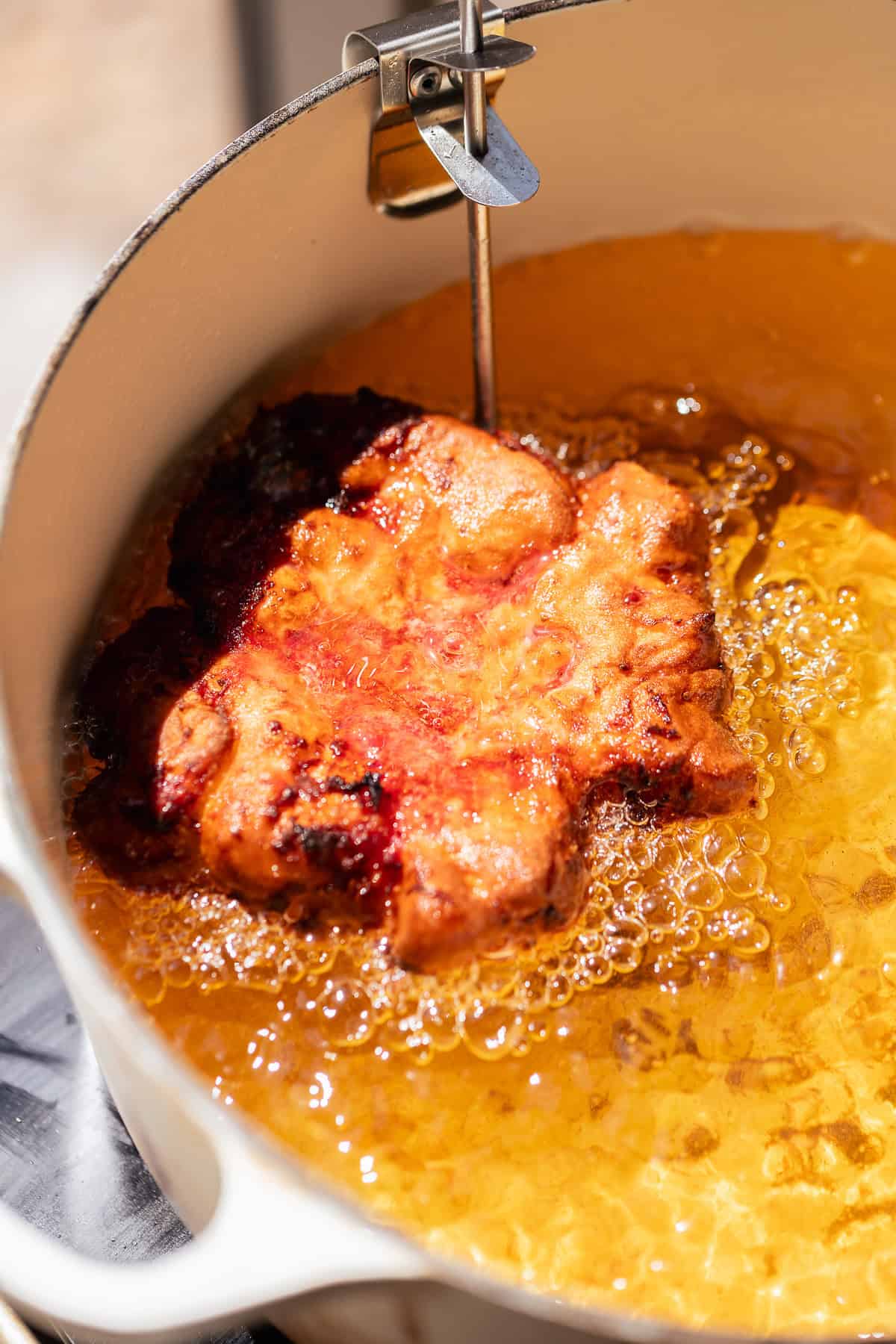 A strawberry fritter frying in hot oil until golden brown.
