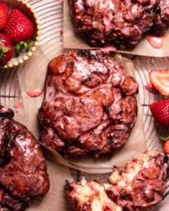 Strawberry fritters topped with a fresh strawberry glaze, served on parchment paper with fresh strawberries and a torn fritter showing the soft interior.