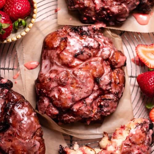 Strawberry fritters topped with a fresh strawberry glaze, served on parchment paper with fresh strawberries and a torn fritter showing the soft interior.