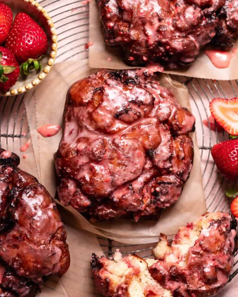Strawberry fritters topped with a fresh strawberry glaze, served on parchment paper with fresh strawberries and a torn fritter showing the soft interior.