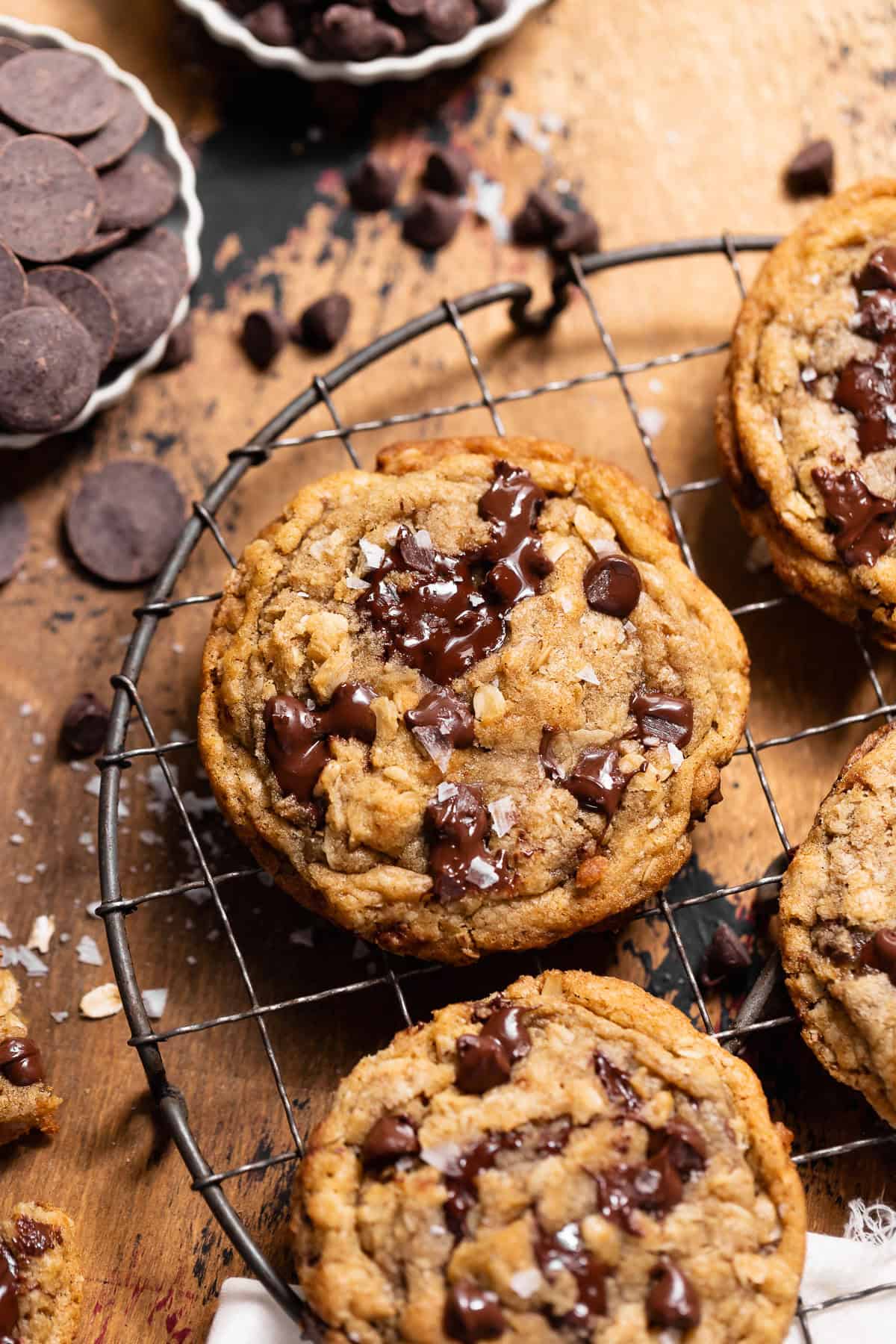 Brown butter oatmeal chocolate chip cookie topped with melted chocolate and flaky sea salt on a cooling rack.