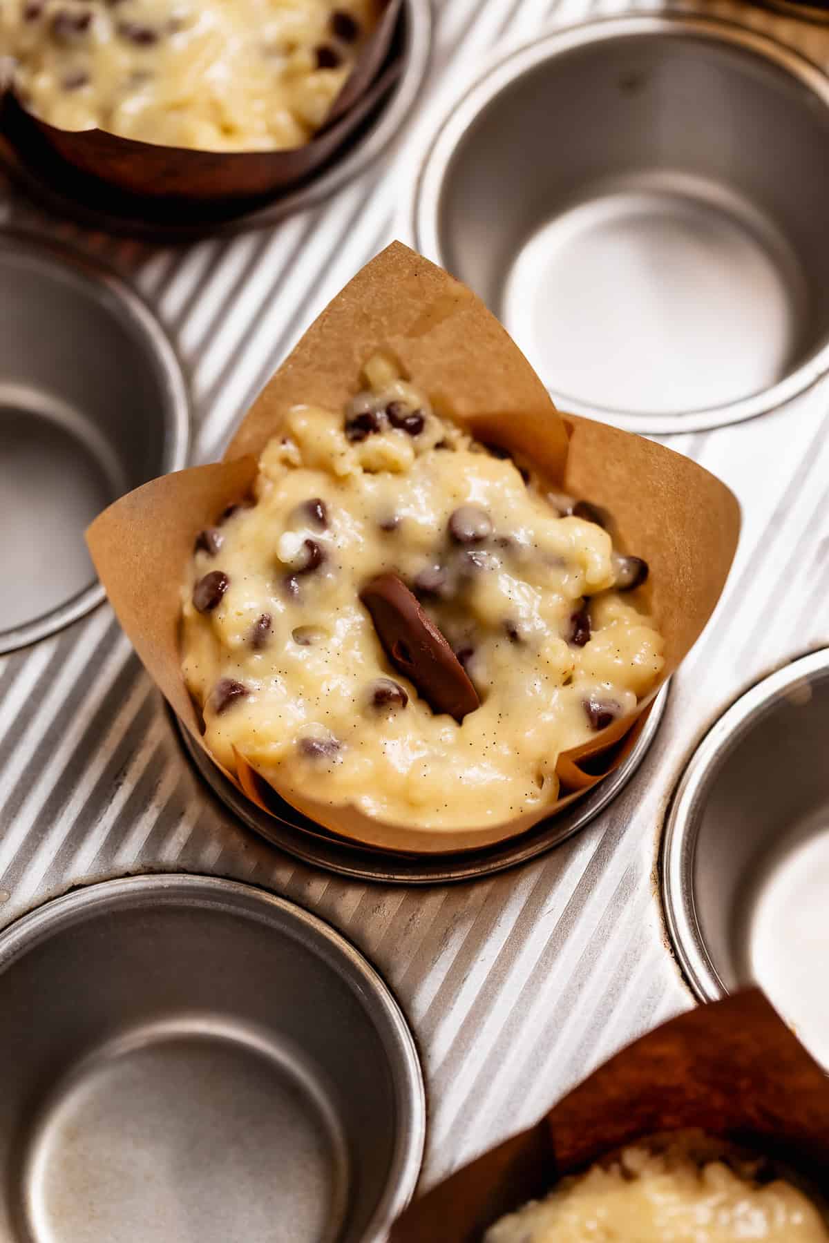 Muffin batter in a tulip muffin liner studded with chocolate chips and topped with a frozen Nutella dollop.