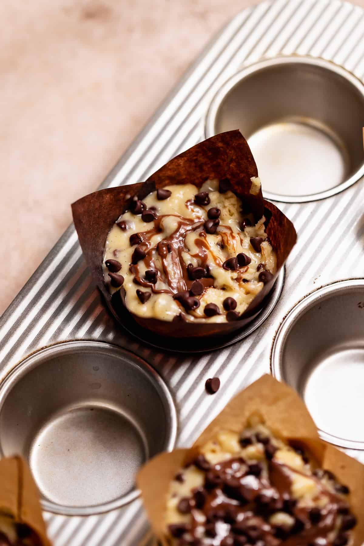 Unbaked stuffed Nutella muffins topped with Nutella swirls and mini chocolate chips in tulip liners.