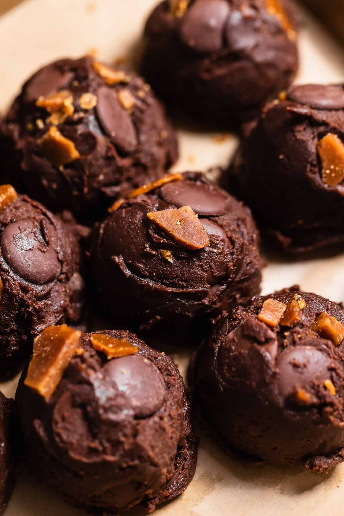 Scooped chocolate cookie dough balls topped with chocolate wafers and toffee pieces before baking.