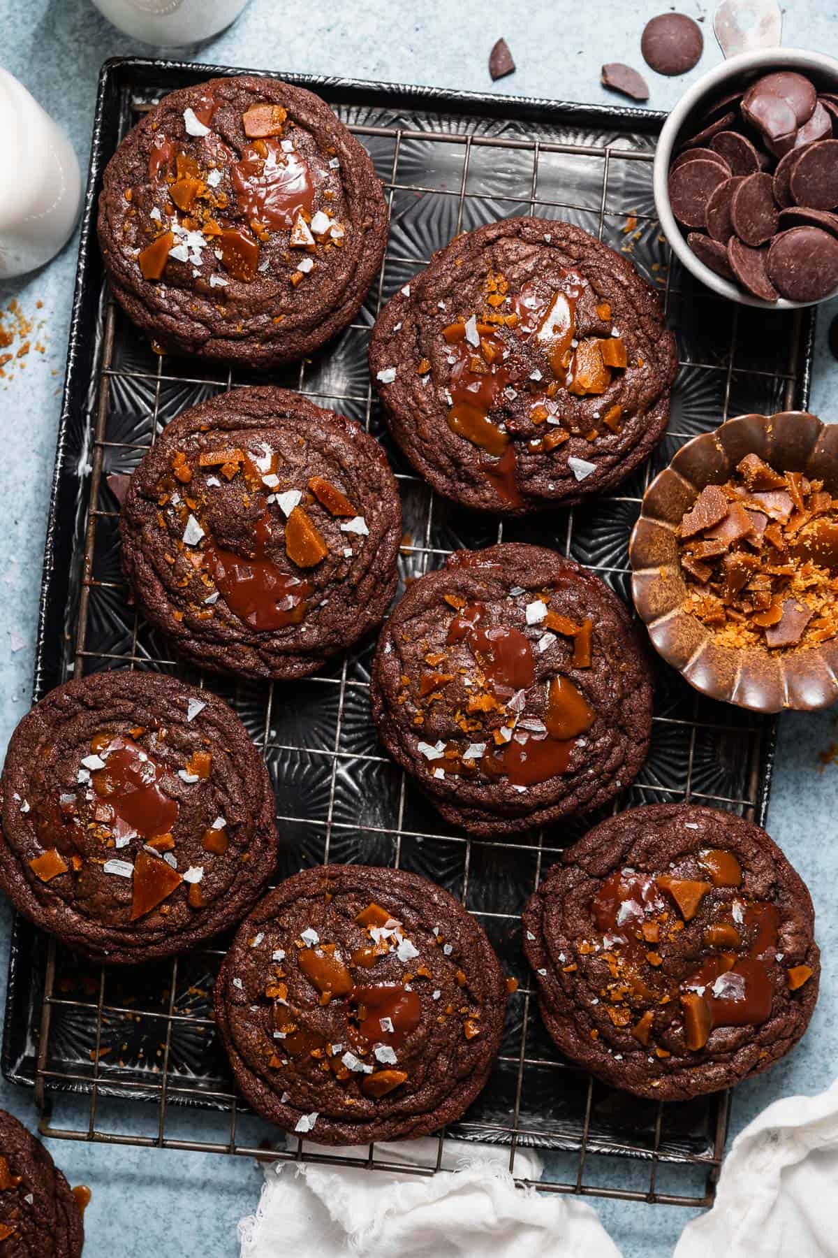 Double chocolate toffee cookies topped with melted chocolate, homemade toffee, and flaky sea salt on a cooling rack.