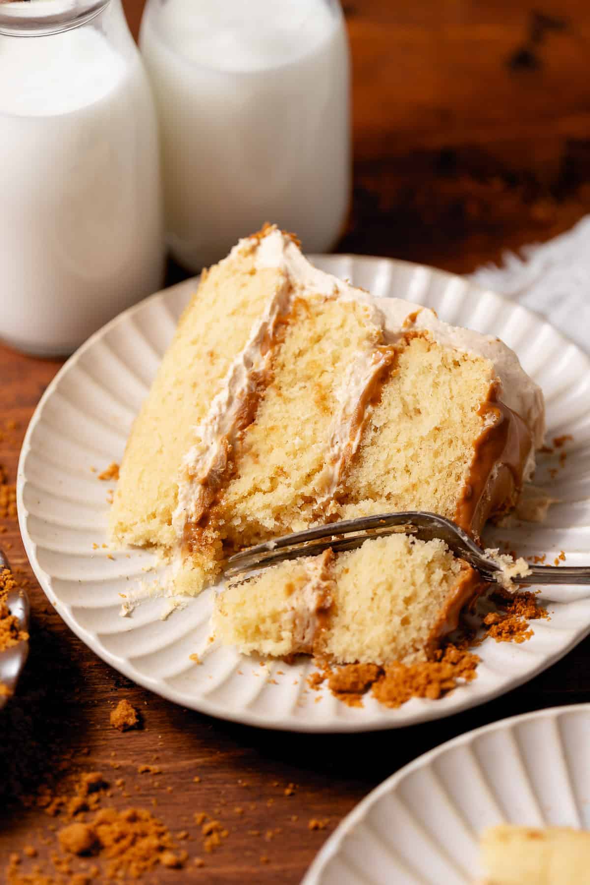 Slice of Biscoff cake with three vanilla cake layers, cookie butter frosting, and Biscoff spread between the layers.