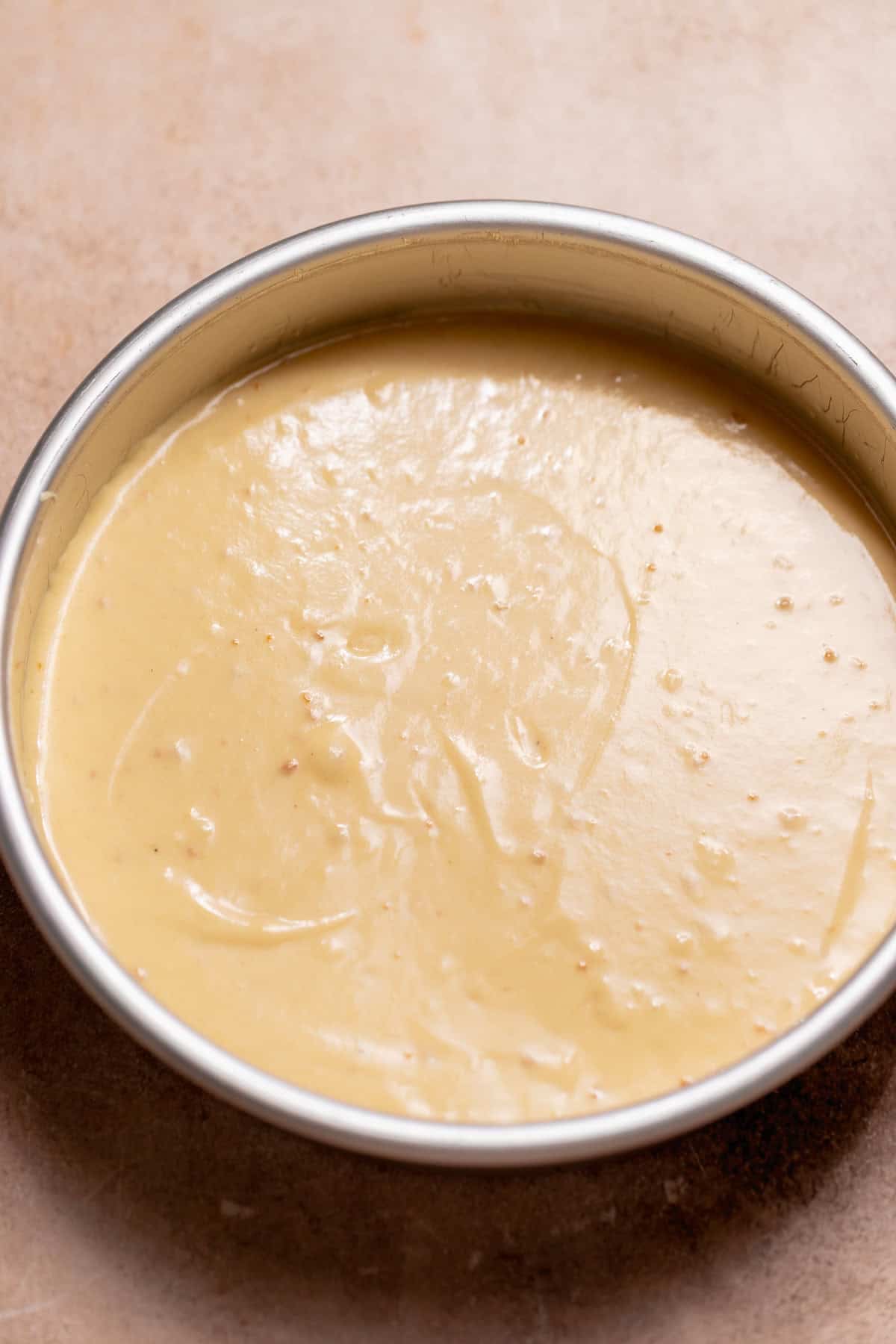 Pale cake batter spread evenly inside a round metal cake pan before baking.