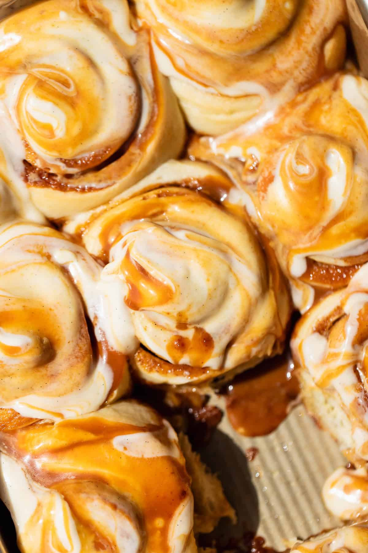Overhead view of caramel cinnamon rolls with caramel vanilla bean cream cheese frosting swirled with salted caramel in a baking pan.