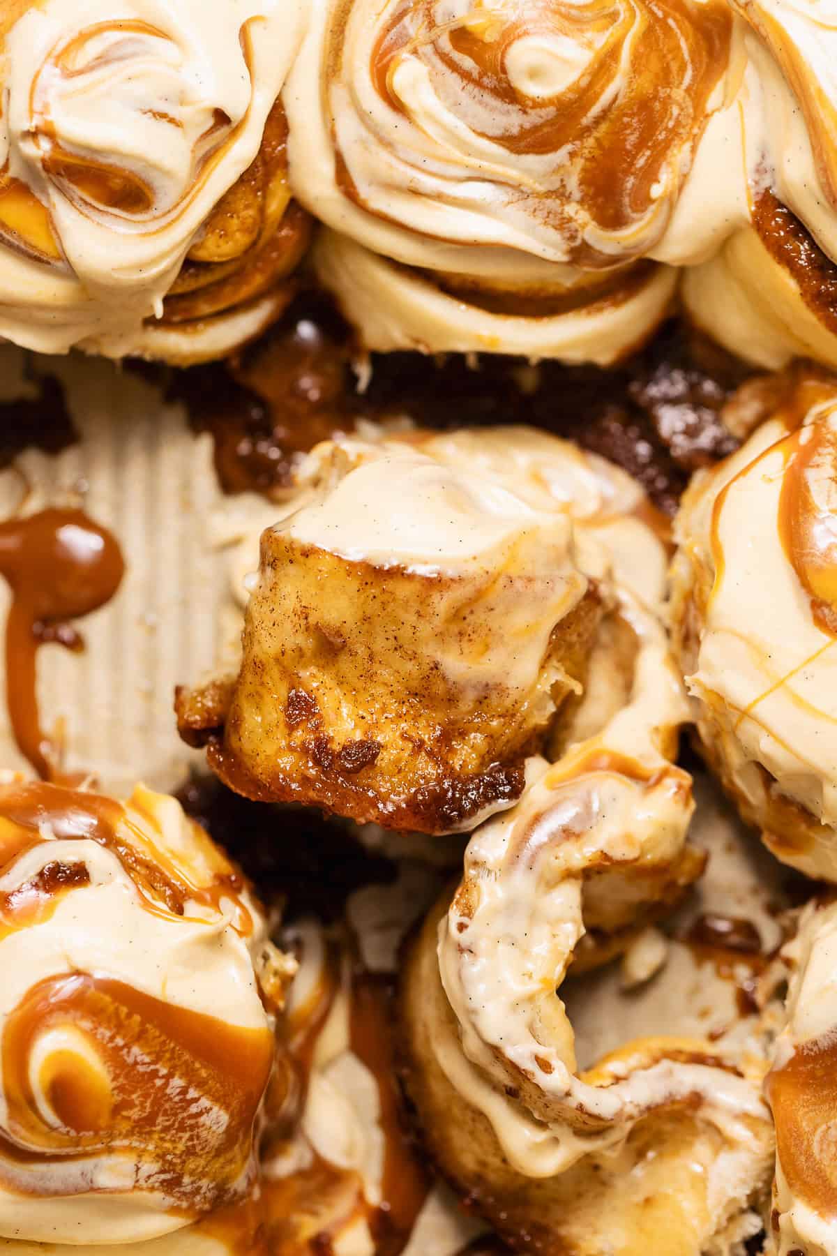 A bite of a caramel roll center showing the soft interior, caramel filling, and cream cheese frosting.