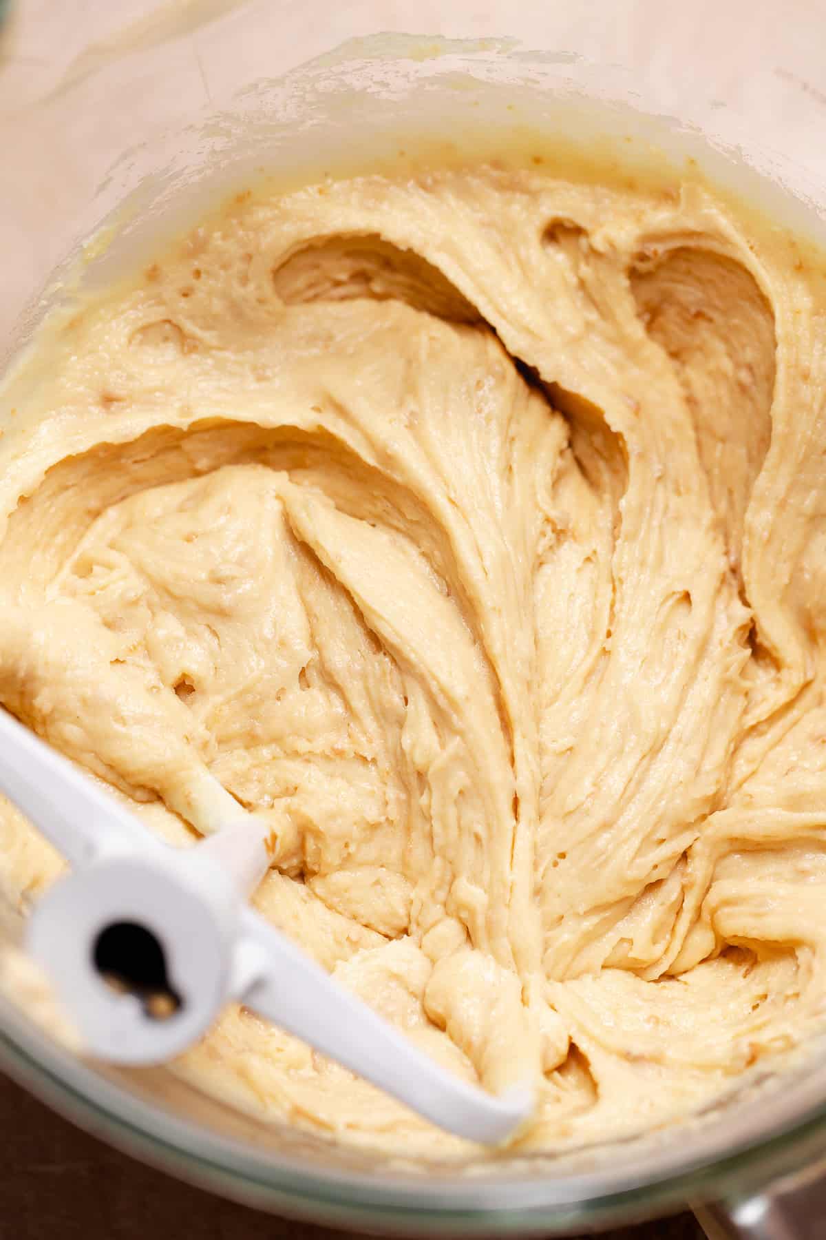 Thick cake batter partially mixed in a glass bowl with a paddle attachment.