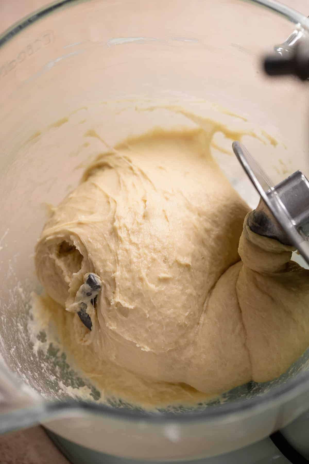 Smooth elastic yeast donut dough wrapped around the dough hook in a stand mixer bowl.