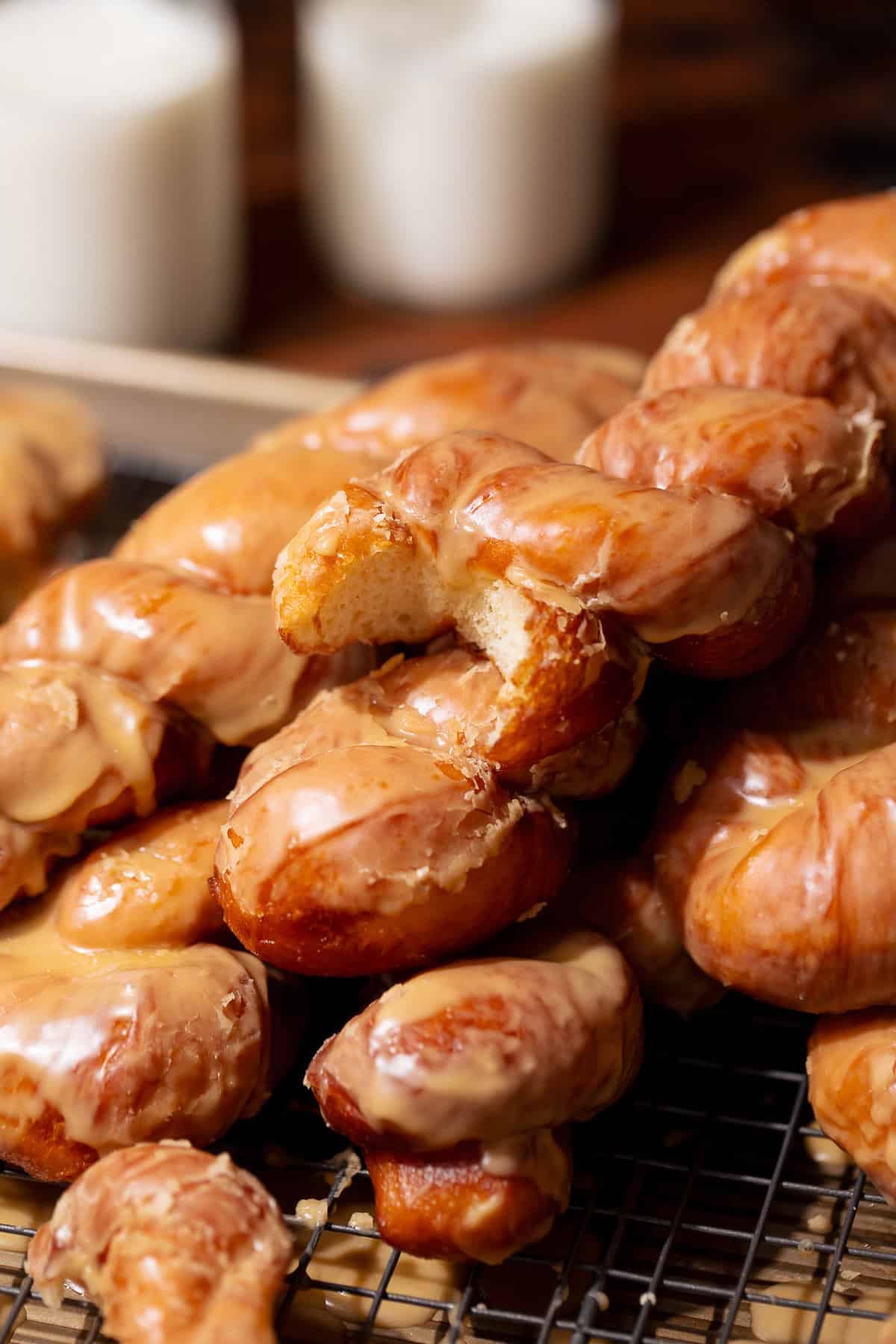Maple glazed donut twists piled on a cooling rack with one torn open to show the soft, fluffy interior.