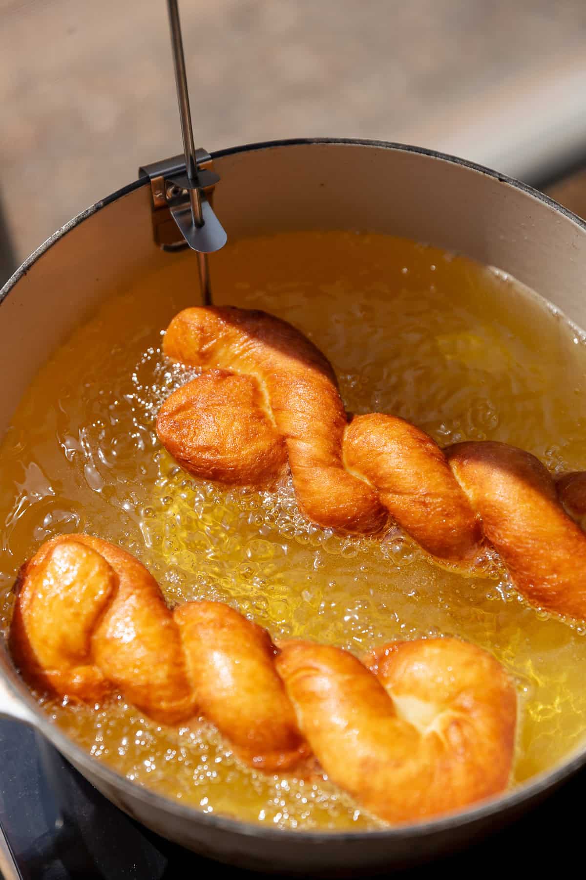 Twisted yeast donuts frying in hot oil until puffed and golden brown.