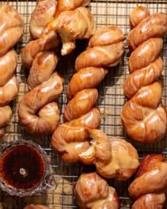 Maple bar donut twists covered in a glossy maple glaze on a cooling rack.