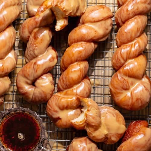 Maple bar donut twists covered in a glossy maple glaze on a cooling rack.
