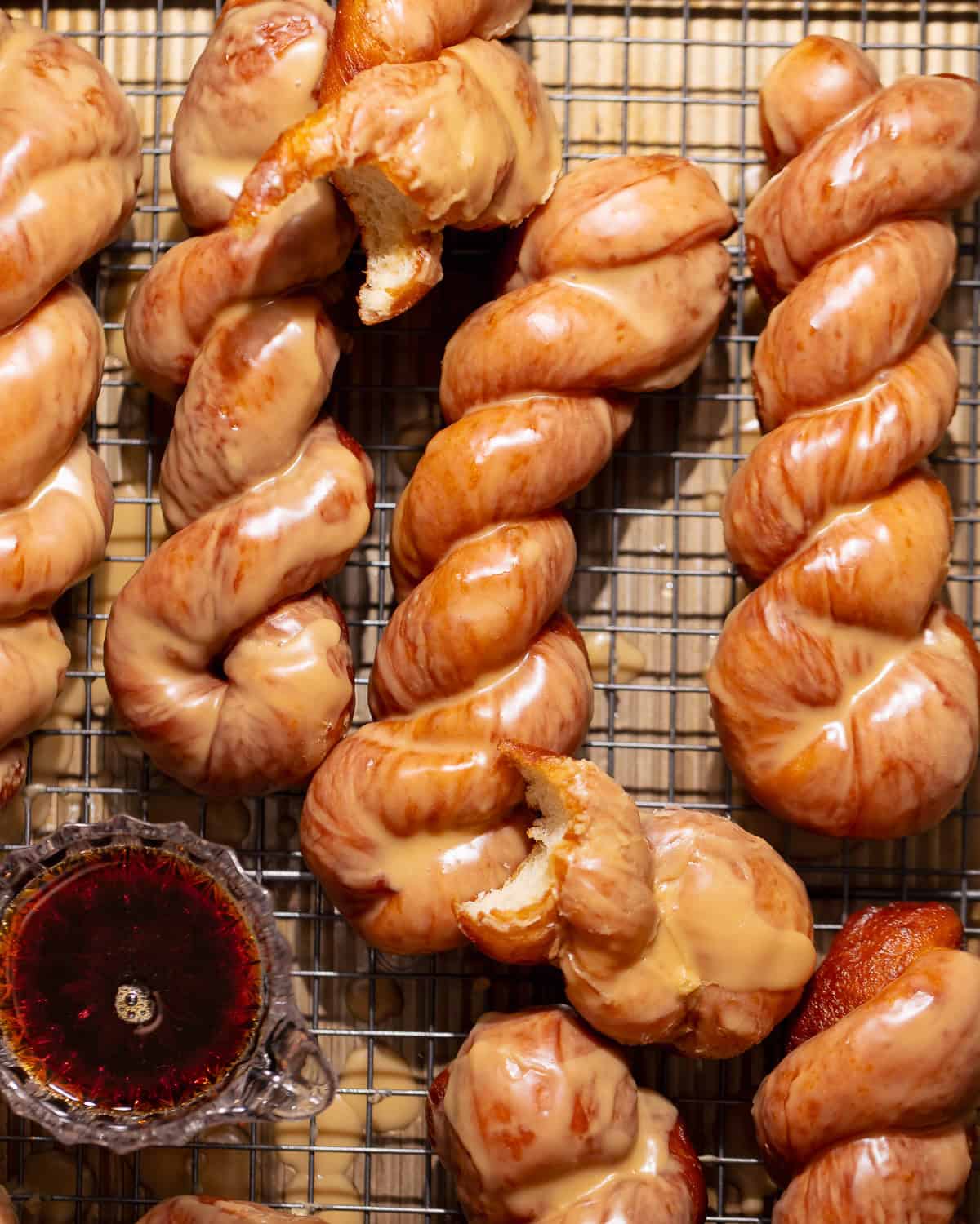 Maple bar donut twists covered in a glossy maple glaze on a cooling rack.