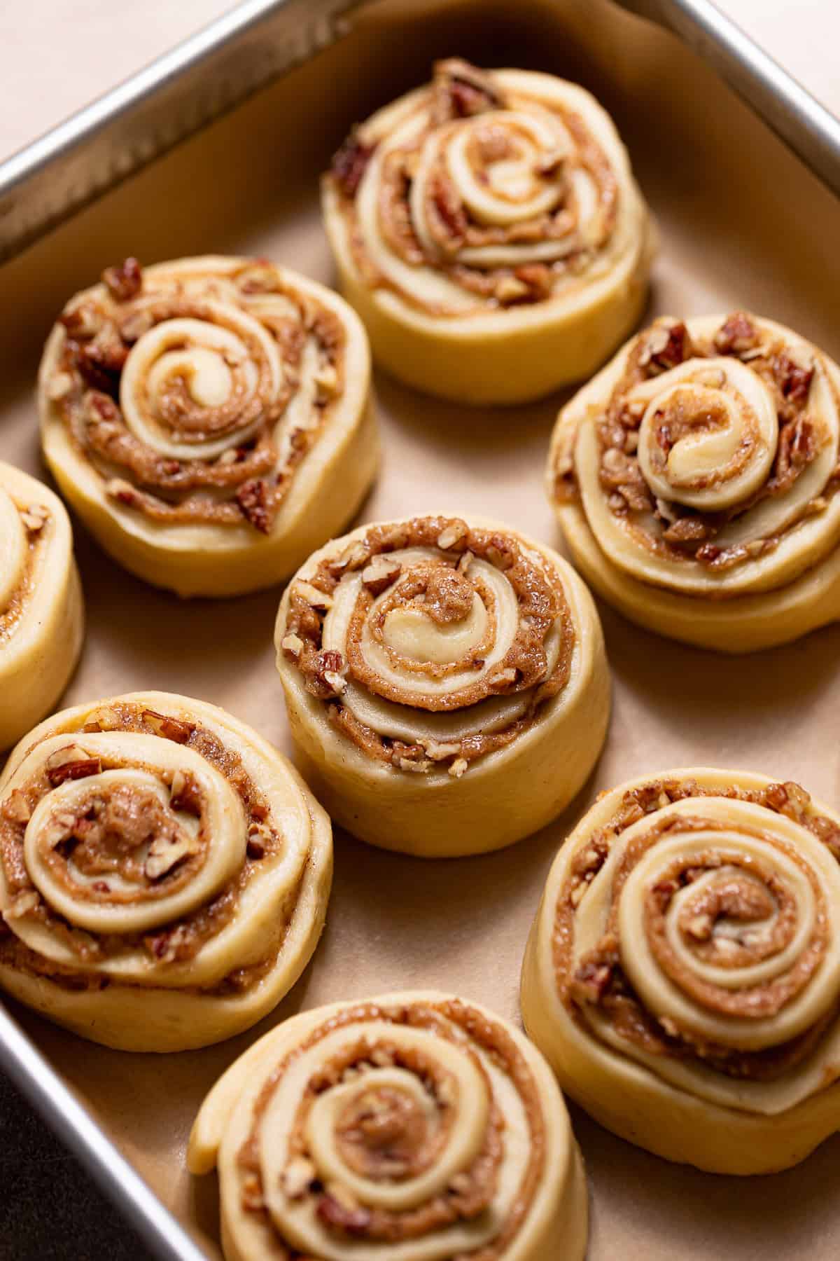 Shaped pecan cinnamon rolls arranged in a baking pan before proofing and baking.