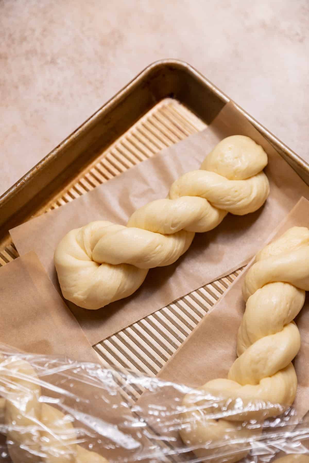 Proofed twisted donut dough resting on individual parchment squares before frying.